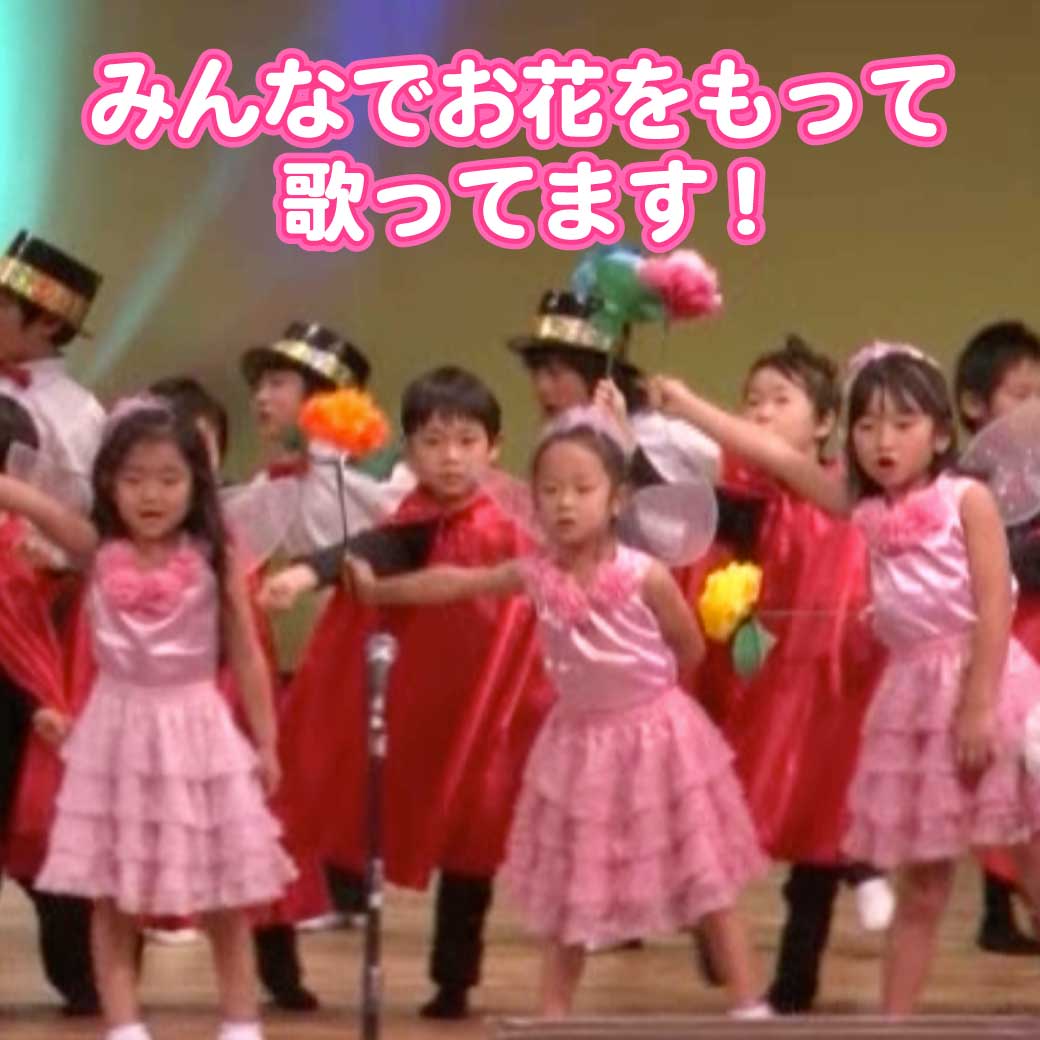 フラワーに扮したこども達がお花を持って歌っている写真